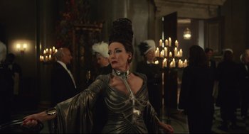 Movie still from “Cruella” (2021), directed by Craig Gillespie – A woman wearing a silver dress and a black hat; Medium shot, Over the shoulder angle