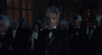 Movie still from “Cruella” (2021), directed by Craig Gillespie – A man in a suit standing in front of a group of people; Close Up shot, Over the shoulder angle