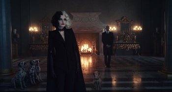 Movie still from “Cruella” (2021), directed by Craig Gillespie – A woman dressed in black standing in front of a fireplace; Wide shot, Over the shoulder angle