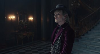 Movie still from “Cruella” (2021), directed by Craig Gillespie – A woman wearing a purple jacket and a hat; Medium shot, Over the shoulder angle