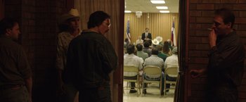 Movie still from “Dallas Buyers Club” (2013), directed by Jean-Marc Vallée – A group of people sitting in front of a microphone in a room; Medium shot, Over the shoulder angle