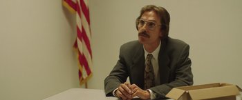 Movie still from “Dallas Buyers Club” (2013), directed by Jean-Marc Vallée – A man sitting at a table in front of an american flag; Medium shot, Over the shoulder angle