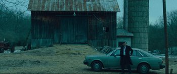 Movie still from “Dark Waters” (2019), directed by Todd Haynes – A man standing next to a car in front of a barn; Wide shot, Low angle