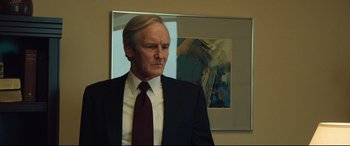 Movie still from “Dark Waters” (2019), directed by Todd Haynes – A man in a suit and tie standing in front of a painting; Medium shot, Low angle