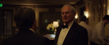 Movie still from “Dark Waters” (2019), directed by Todd Haynes – A man in a tuxedo standing next to another man in a suit; Medium shot, Over the shoulder angle