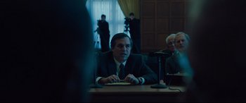 Movie still from “Dark Waters” (2019), directed by Todd Haynes – A man sitting at a table in front of microphones; Medium shot, Over the shoulder angle