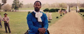 Movie still from “Django Unchained” (2012), directed by Quentin Tarantino – A man in a blue shirt sitting in a field; Medium shot, Over the shoulder angle