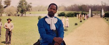 Movie still from “Django Unchained” (2012), directed by Quentin Tarantino – A man sitting on a chair in a field with other people in the background; Medium shot, Over the shoulder angle