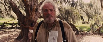 Movie still from “Django Unchained” (2012), directed by Quentin Tarantino – An older man with a beard and a newspaper on his shirt; Medium shot, Low angle