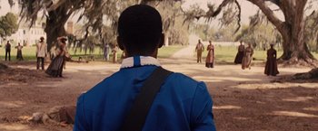 Movie still from “Django Unchained” (2012), directed by Quentin Tarantino – A man standing in front of a group of people on a dirt road; Medium shot, Over the shoulder angle
