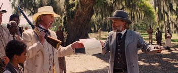 Movie still from “Django Unchained” (2012), directed by Quentin Tarantino – A man in a hat is handing a piece of paper to another man in a suit; Medium shot, Over the shoulder angle