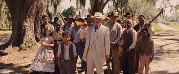 Movie still from “Django Unchained” (2012), directed by Quentin Tarantino – A man in a suit and hat stands in front of a group of people; Wide shot, Low angle