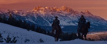 A man riding a horse in the snow at sunset