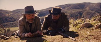 Movie still from “Django Unchained” (2012), directed by Quentin Tarantino – A couple of men sitting on top of a grass covered field; Medium shot, High angle