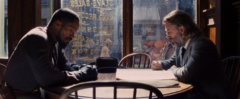 Movie still from “Django Unchained” (2012), directed by Quentin Tarantino – Two people sitting at a table in front of a store window; Medium shot, Over the shoulder angle