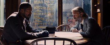 Movie still from “Django Unchained” (2012), directed by Quentin Tarantino – Two people sitting at a table in front of a store window; Medium shot, Over the shoulder angle