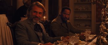 Movie still from “Django Unchained” (2012), directed by Quentin Tarantino – Two men sitting at a dinner table with a candle in the background; Medium shot, Over the shoulder angle