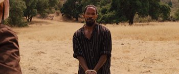 Movie still from “Django Unchained” (2012), directed by Quentin Tarantino – A man in striped shirt standing in a field with hands tied; Medium shot, Over the shoulder angle