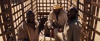Movie still from “Django Unchained” (2012), directed by Quentin Tarantino – A group of men sitting next to each other on the ground; Medium shot, High angle