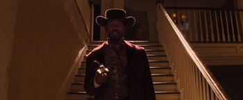 Movie still from “Django Unchained” (2012), directed by Quentin Tarantino – A man wearing a hat and a suit standing in front of a staircase; Medium shot, Low angle