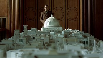 Movie still from “Downfall” (2004), directed by Oliver Hirschbiegel – A man standing in front of a model of the capitol building; Wide shot, Over the shoulder angle