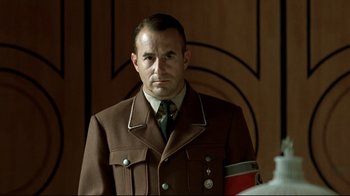 Movie still from “Downfall” (2004), directed by Oliver Hirschbiegel – A man in a military uniform is standing in front of a wall; Close Up shot, Over the shoulder angle