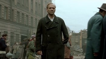 Movie still from “Downfall” (2004), directed by Oliver Hirschbiegel – A man in a trench coat standing in the middle of a street; Medium shot, Low angle