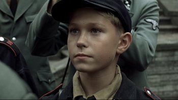 Movie still from “Downfall” (2004), directed by Oliver Hirschbiegel – A young boy wearing a black hat and jacket; Close Up shot, High angle