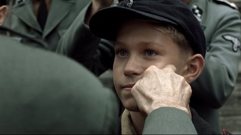Movie still from “Downfall” (2004), directed by Oliver Hirschbiegel – A young boy wearing a hat and holding his hand to his face; Close Up shot, Over the shoulder angle