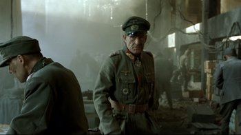 Movie still from “Downfall” (2004), directed by Oliver Hirschbiegel – An older man in a military uniform stands next to a building; Medium shot, Over the shoulder angle