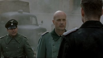 Movie still from “Downfall” (2004), directed by Oliver Hirschbiegel – A man in a military uniform standing in front of other men; Close Up shot, Over the shoulder angle