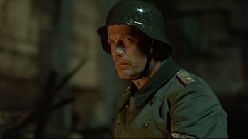 Movie still from “Downfall” (2004), directed by Oliver Hirschbiegel – A man in a uniform and a helmet is looking at the camera; Close Up shot, Over the shoulder angle
