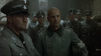 Movie still from “Downfall” (2004), directed by Oliver Hirschbiegel – A group of men in uniforms are standing in a room; Medium shot, Over the shoulder angle