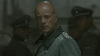 Movie still from “Downfall” (2004), directed by Oliver Hirschbiegel – A bald man in a military uniform is standing in front of a group of soldiers; Close Up shot, Over the shoulder angle