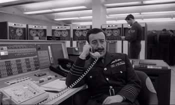 Movie still from “Dr. Strangelove or: How I Learned to Stop Worrying and Love the Bomb” (1964), directed by Stanley Kubrick – A man sitting at a desk talking on a phone; Medium shot, Low angle