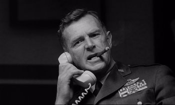 Movie still from “Dr. Strangelove or: How I Learned to Stop Worrying and Love the Bomb” (1964), directed by Stanley Kubrick – An old photo of an older man smoking a cigarette while holding a phone to his ear; Close Up shot, Low angle