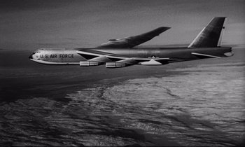 Movie still from “Dr. Strangelove or: How I Learned to Stop Worrying and Love the Bomb” (1964), directed by Stanley Kubrick – An air force plane flying over a body of water; Wide shot, Low angle