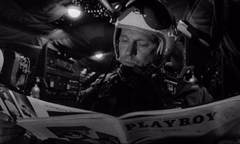 Movie still from “Dr. Strangelove or: How I Learned to Stop Worrying and Love the Bomb” (1964), directed by Stanley Kubrick – A man wearing a helmet and reading a magazine; Close Up shot, Low angle