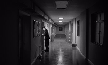 Movie still from “Dr. Strangelove or: How I Learned to Stop Worrying and Love the Bomb” (1964), directed by Stanley Kubrick – A man standing in an empty room looking at a bulletin board; Extreme Wide shot, High angle