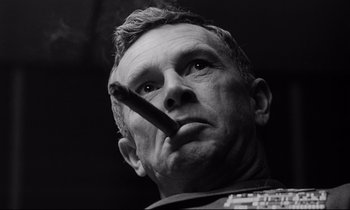 Movie still from “Dr. Strangelove or: How I Learned to Stop Worrying and Love the Bomb” (1964), directed by Stanley Kubrick – An older man smoking a cigarette while looking at the camera; Close Up shot, Low angle