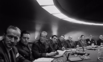 Movie still from “Dr. Strangelove or: How I Learned to Stop Worrying and Love the Bomb” (1964), directed by Stanley Kubrick – A black and white photo of a group of men sitting at a table; Medium shot, Low angle