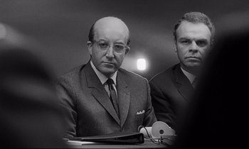Movie still from “Dr. Strangelove or: How I Learned to Stop Worrying and Love the Bomb” (1964), directed by Stanley Kubrick – A man in a suit sitting next to another man in a suit; Close Up shot, Over the shoulder angle