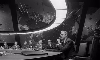 Movie still from “Dr. Strangelove or: How I Learned to Stop Worrying and Love the Bomb” (1964), directed by Stanley Kubrick – A group of men sitting at a table in front of a map; Wide shot, Low angle
