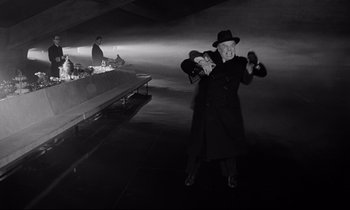 Movie still from “Dr. Strangelove or: How I Learned to Stop Worrying and Love the Bomb” (1964), directed by Stanley Kubrick – A man in a black coat and a black hat; Wide shot, Low angle