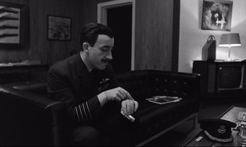 Movie still from “Dr. Strangelove or: How I Learned to Stop Worrying and Love the Bomb” (1964), directed by Stanley Kubrick – A black and white photo of a man smoking a cigarette; Medium shot, High angle