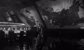 Movie still from “Dr. Strangelove or: How I Learned to Stop Worrying and Love the Bomb” (1964), directed by Stanley Kubrick – A black and white photo of a man in a suit walking in front of a map; Extreme Wide shot, Low angle