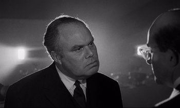 Movie still from “Dr. Strangelove or: How I Learned to Stop Worrying and Love the Bomb” (1964), directed by Stanley Kubrick – An older man in a suit and tie; Close Up shot, Over the shoulder angle