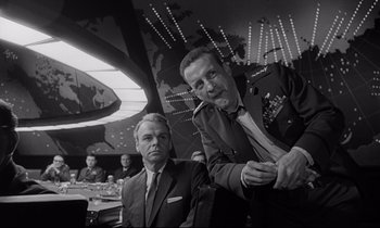 Movie still from “Dr. Strangelove or: How I Learned to Stop Worrying and Love the Bomb” (1964), directed by Stanley Kubrick – Two men in suits are sitting at a table; Medium shot, Low angle