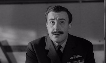 Movie still from “Dr. Strangelove or: How I Learned to Stop Worrying and Love the Bomb” (1964), directed by Stanley Kubrick – An older man in a suit and tie with a mustache; Close Up shot, Low angle
