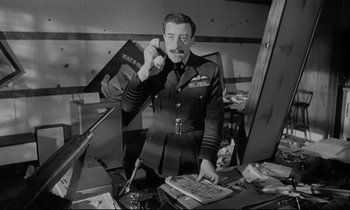 Movie still from “Dr. Strangelove or: How I Learned to Stop Worrying and Love the Bomb” (1964), directed by Stanley Kubrick – An old photo of a man in a military uniform; Medium shot, Low angle